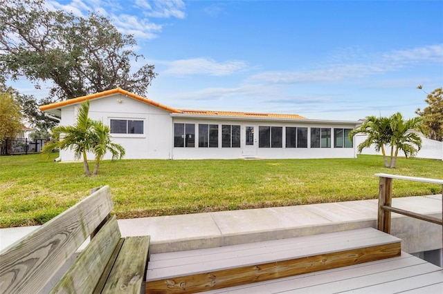 rear view of house with a sunroom, a deck, and a lawn