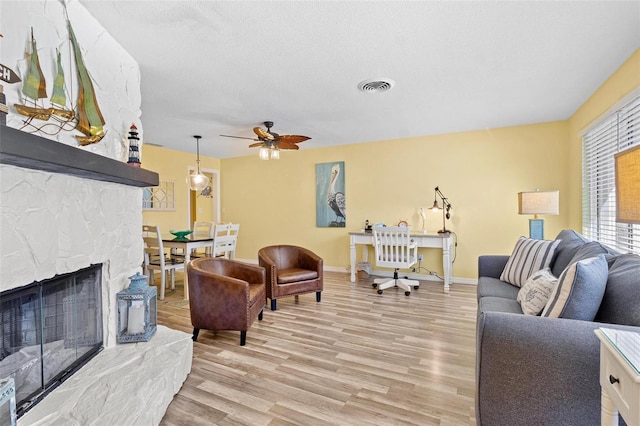 living room featuring ceiling fan, light wood-type flooring, a textured ceiling, and a fireplace