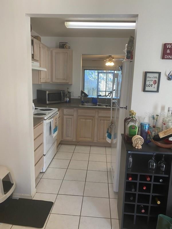 kitchen featuring light tile patterned flooring, white appliances, light brown cabinetry, and sink