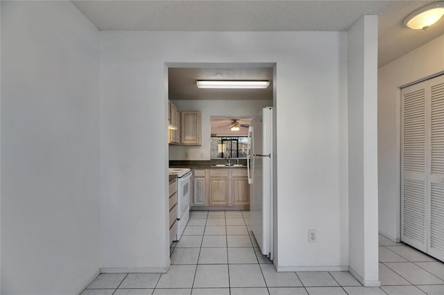 kitchen featuring white appliances, dark countertops, light brown cabinetry, a sink, and light tile patterned flooring