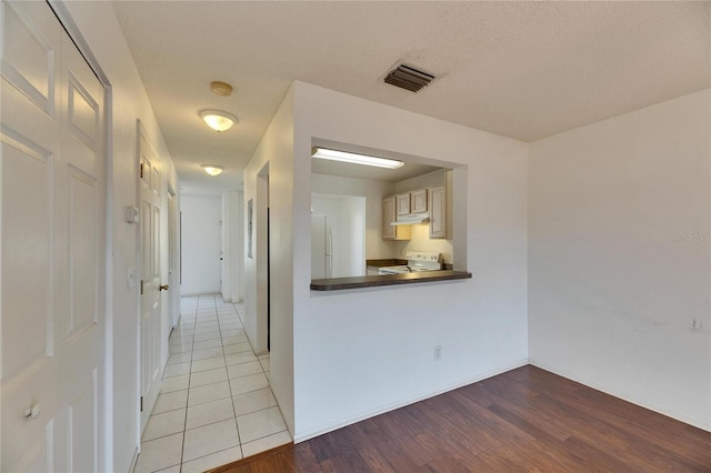 hall with light wood-type flooring, visible vents, and a textured ceiling