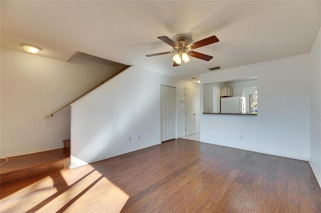 unfurnished living room featuring visible vents, a ceiling fan, stairway, wood finished floors, and a textured ceiling