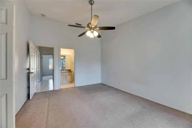 unfurnished bedroom with light tile patterned floors, ensuite bathroom, a ceiling fan, and light colored carpet