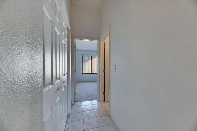 hall with light colored carpet and light tile patterned floors