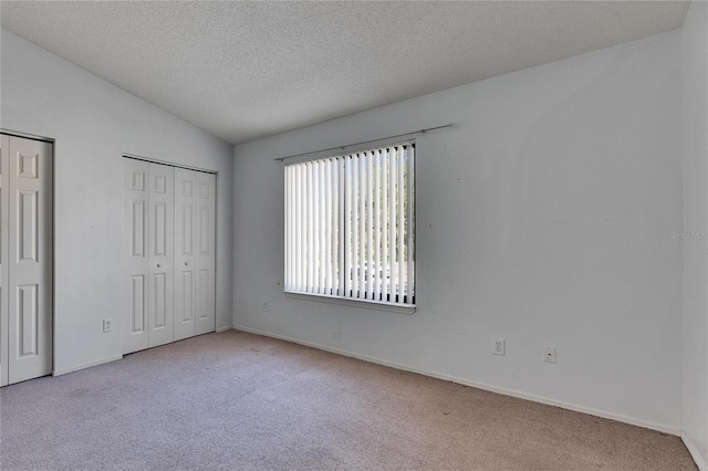 unfurnished bedroom with baseboards, vaulted ceiling, a textured ceiling, carpet floors, and two closets