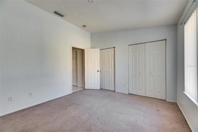 unfurnished bedroom featuring baseboards, visible vents, light colored carpet, a textured ceiling, and two closets