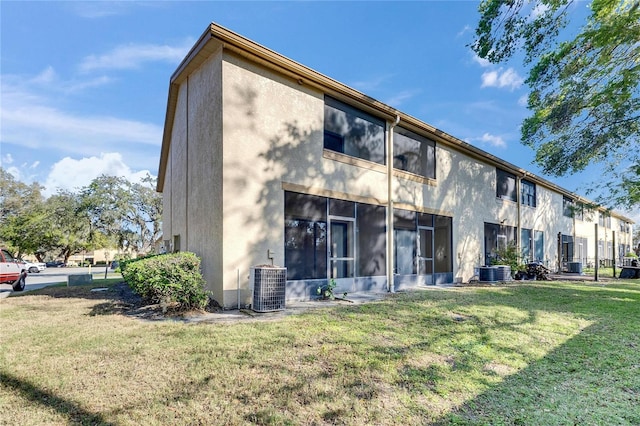 rear view of house with cooling unit, a lawn, and stucco siding