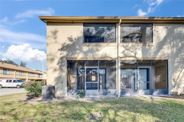 back of property featuring central air condition unit, a sunroom, a lawn, and stucco siding