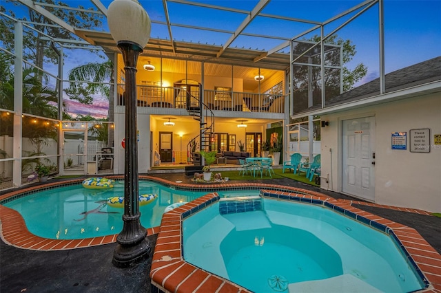 pool at dusk with an in ground hot tub, a patio area, and a lanai