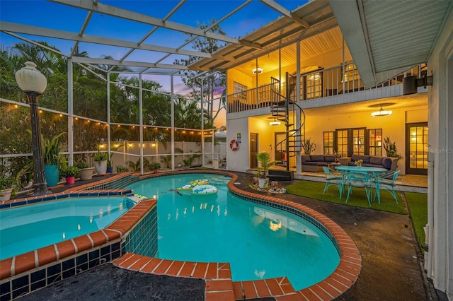 pool at dusk with glass enclosure, a patio area, outdoor lounge area, and ceiling fan