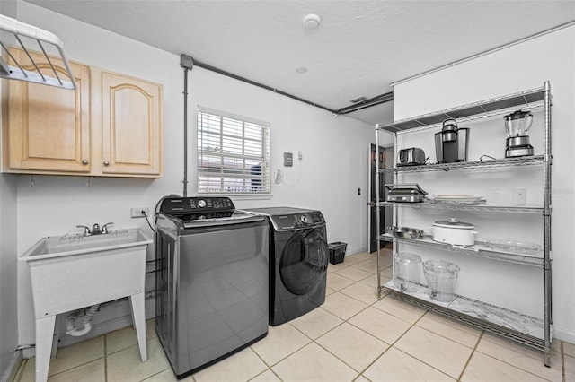 laundry area with a textured ceiling, light tile patterned floors, sink, washing machine and dryer, and cabinets