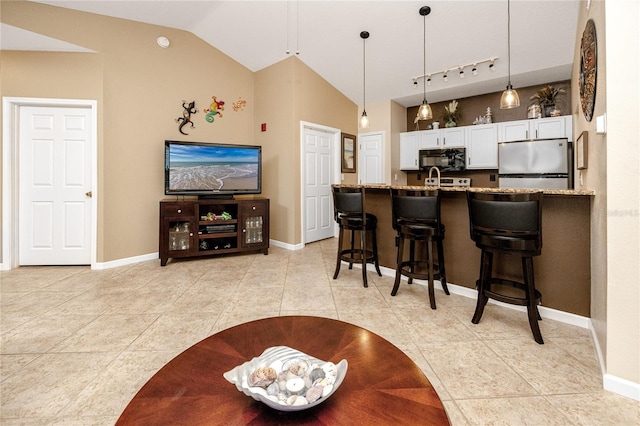 kitchen featuring a kitchen bar, white cabinetry, hanging light fixtures, stainless steel fridge, and light stone countertops