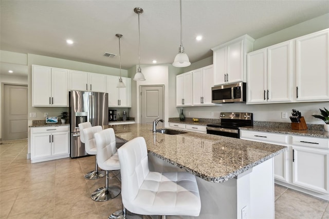 kitchen featuring a center island with sink, visible vents, a sink, stainless steel appliances, and white cabinetry