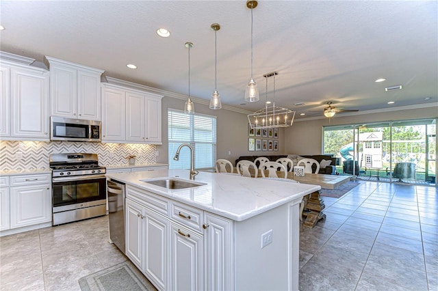 kitchen with appliances with stainless steel finishes, sink, white cabinets, backsplash, and a center island with sink