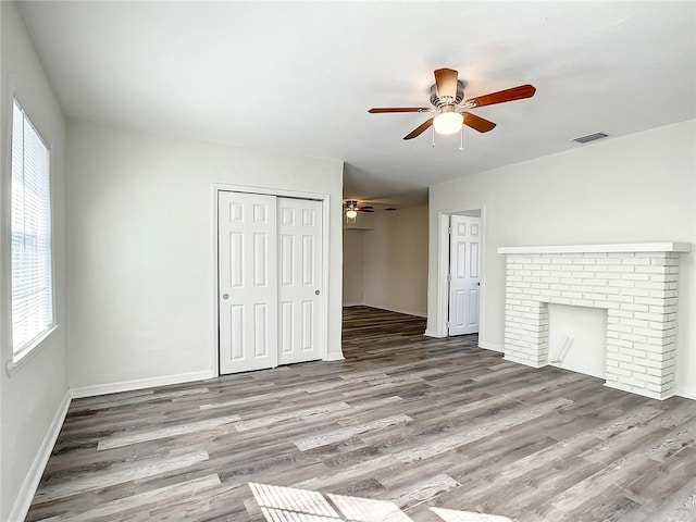 unfurnished living room featuring a brick fireplace, hardwood / wood-style flooring, and ceiling fan