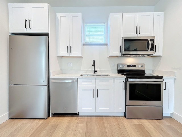 kitchen with appliances with stainless steel finishes, sink, white cabinets, and light hardwood / wood-style floors