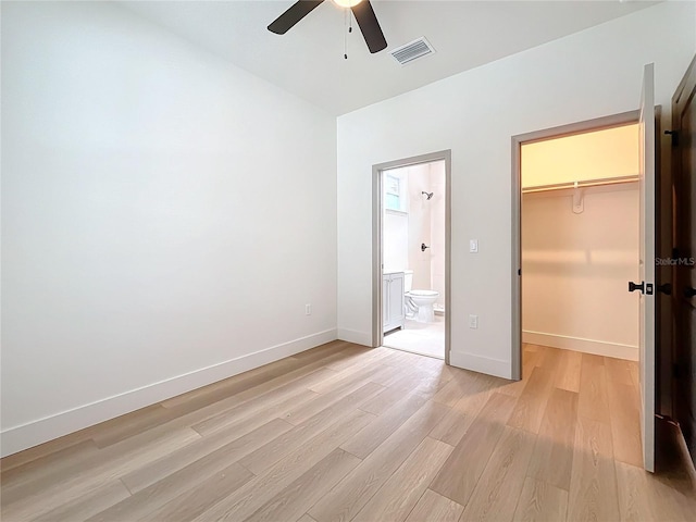 unfurnished bedroom with ensuite bathroom, a spacious closet, light wood-type flooring, a closet, and ceiling fan