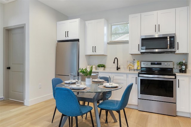 kitchen with stainless steel appliances, white cabinetry, sink, and light hardwood / wood-style flooring