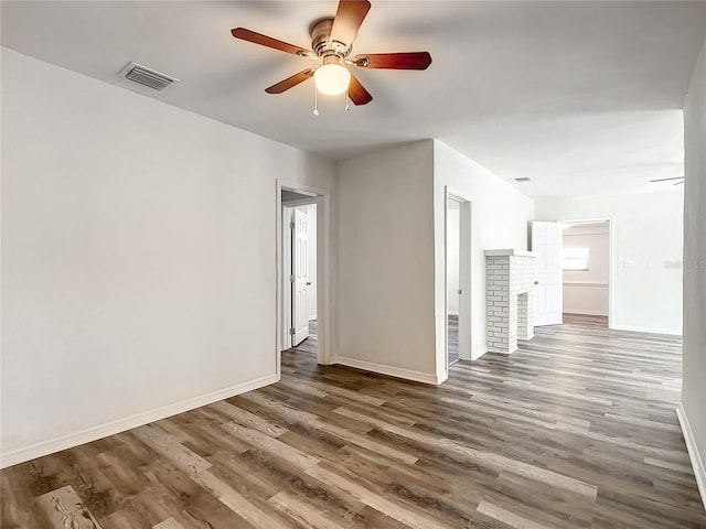 empty room featuring ceiling fan, a fireplace, and dark hardwood / wood-style flooring