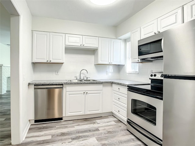 kitchen with sink, white cabinetry, light stone counters, light wood-type flooring, and appliances with stainless steel finishes