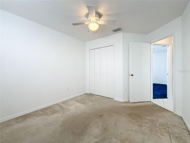 unfurnished bedroom with ceiling fan, light colored carpet, a closet, and a textured ceiling