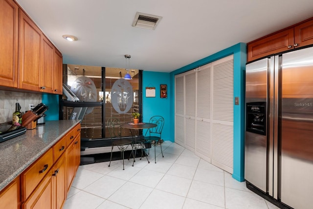 kitchen featuring stainless steel refrigerator with ice dispenser, decorative light fixtures, decorative backsplash, and dark stone countertops