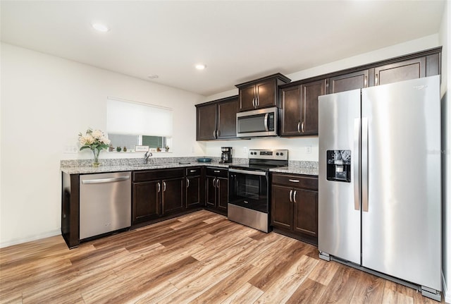 kitchen featuring sink, light wood-type flooring, stainless steel appliances, light stone countertops, and dark brown cabinetry