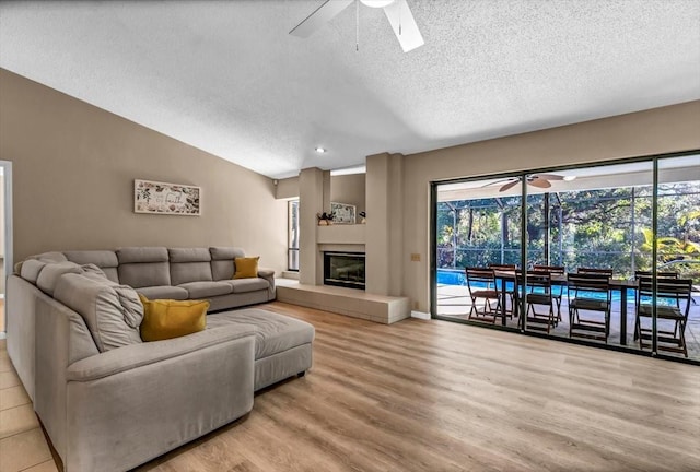 living room featuring vaulted ceiling, a textured ceiling, ceiling fan, and light hardwood / wood-style flooring