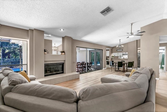 living room featuring hardwood / wood-style floors, a fireplace, a textured ceiling, ceiling fan with notable chandelier, and vaulted ceiling