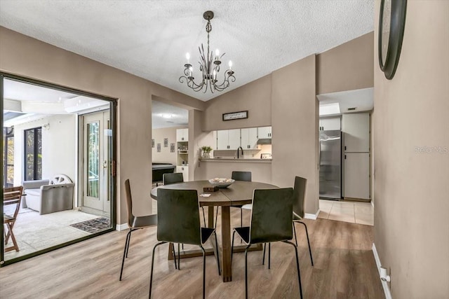 dining space with lofted ceiling, an inviting chandelier, a textured ceiling, and light wood-type flooring