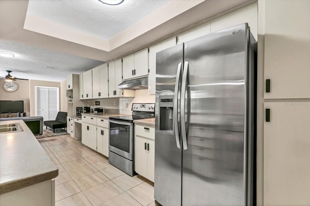 kitchen featuring stainless steel appliances, white cabinetry, light tile patterned flooring, and a tray ceiling