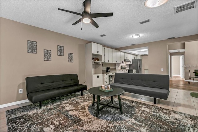 living room featuring ceiling fan, light tile patterned floors, and a textured ceiling