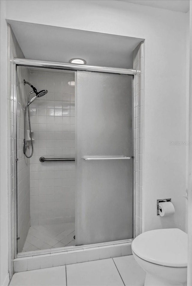 bathroom with tile patterned flooring, a shower with shower door, and toilet