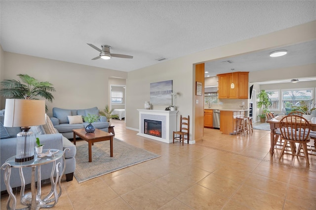 living room featuring light tile patterned flooring, ceiling fan, sink, and a textured ceiling