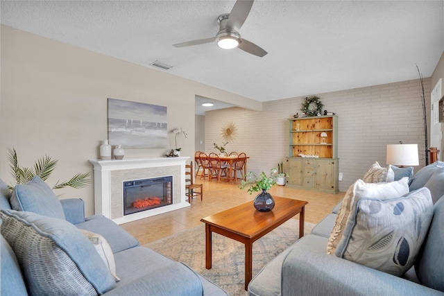 living room featuring light tile patterned flooring, ceiling fan, brick wall, and a textured ceiling