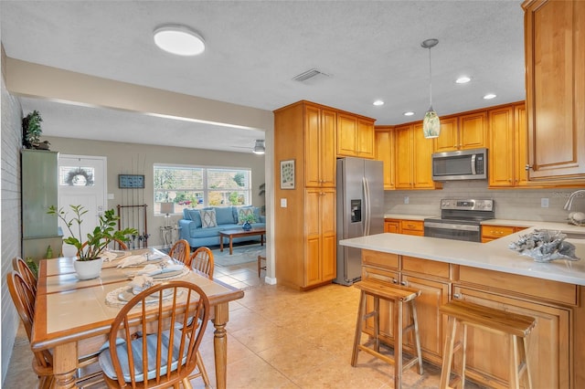 kitchen featuring a breakfast bar, pendant lighting, tasteful backsplash, ceiling fan, and stainless steel appliances