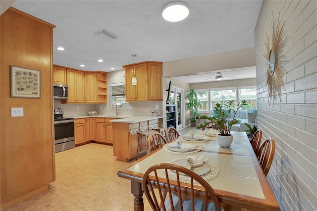 kitchen with sink, kitchen peninsula, ceiling fan, stainless steel appliances, and decorative backsplash