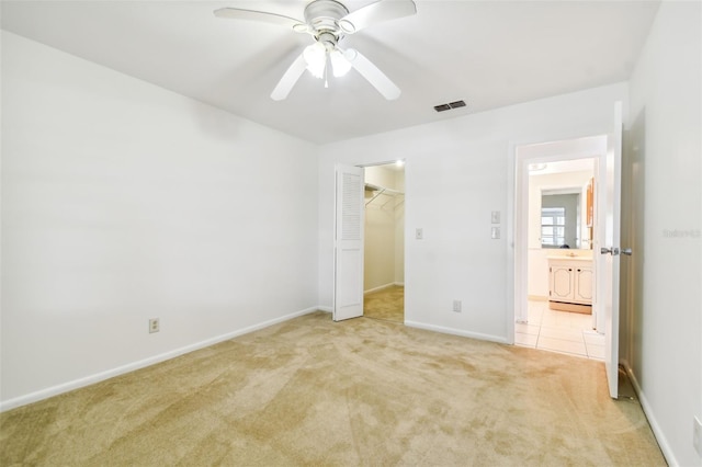 unfurnished bedroom with ceiling fan, a spacious closet, a closet, and light carpet