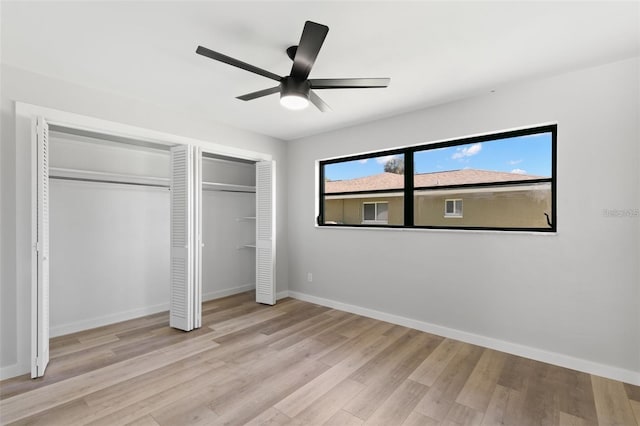 unfurnished bedroom featuring ceiling fan, multiple closets, and light wood-type flooring