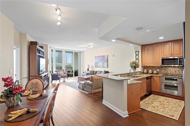 kitchen featuring dark wood-type flooring, appliances with stainless steel finishes, kitchen peninsula, light stone countertops, and backsplash