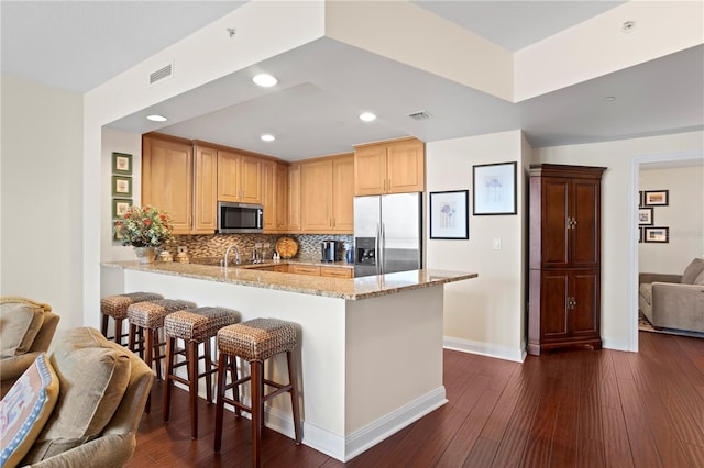 kitchen with appliances with stainless steel finishes, light stone counters, tasteful backsplash, kitchen peninsula, and light brown cabinets