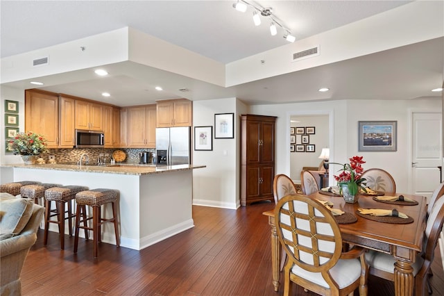 kitchen featuring dark wood-type flooring, appliances with stainless steel finishes, kitchen peninsula, light stone countertops, and decorative backsplash