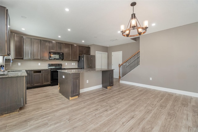 kitchen with hanging light fixtures, sink, light stone counters, a kitchen island, and black appliances