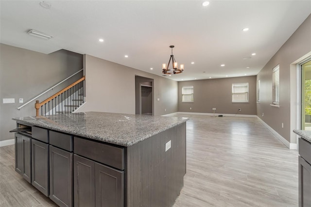 kitchen with dark brown cabinets, hanging light fixtures, light stone countertops, a center island, and light hardwood / wood-style floors