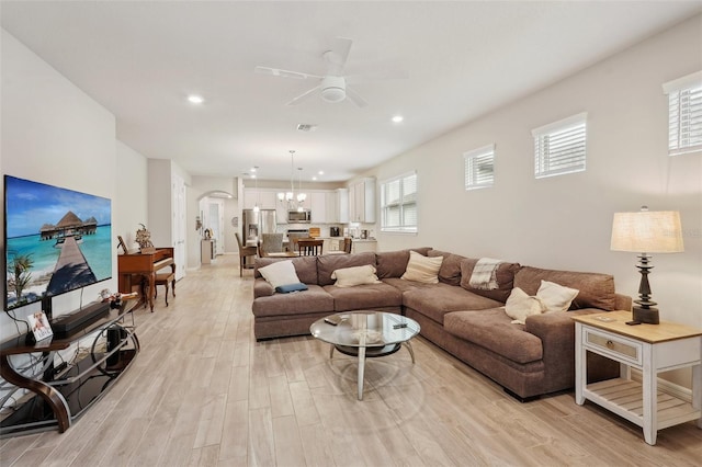 living room featuring ceiling fan with notable chandelier and light wood-type flooring