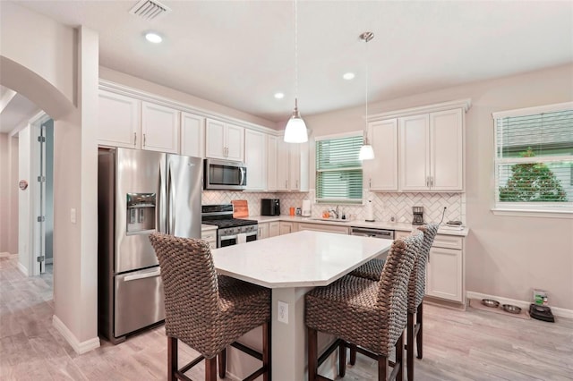 kitchen with a breakfast bar area, appliances with stainless steel finishes, white cabinets, a kitchen island, and decorative light fixtures