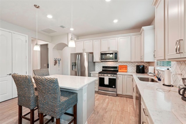 kitchen with appliances with stainless steel finishes, pendant lighting, sink, white cabinets, and a kitchen breakfast bar