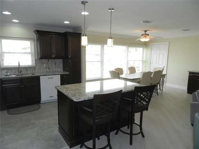 kitchen featuring decorative light fixtures, tasteful backsplash, dishwasher, sink, and a kitchen bar