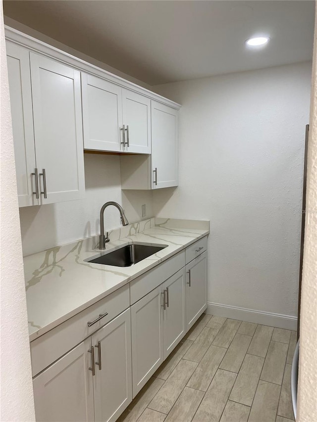 kitchen featuring sink, white cabinetry, and light stone counters