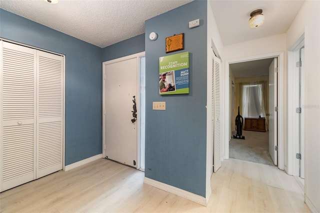 corridor featuring baseboards, a textured ceiling, and light wood finished floors